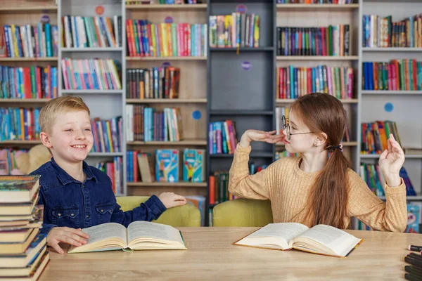 Little school children reading books together while sitting at table in library. Boy and girl study at school. Happy children