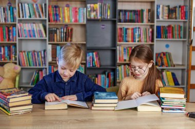 Little school children reading books together while sitting at table in library. Boy and girl study at school. World Book Day