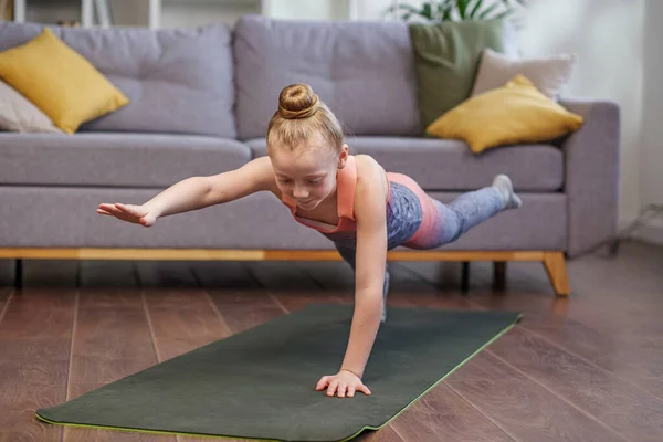 Little girl practicing stretching in room. Physical exercises for children at home. Concept of sports and healthy lifestyle.