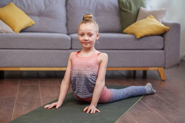 Little girl practicing stretching in room. Physical exercises for children at home. Concept of sports and healthy lifestyle.