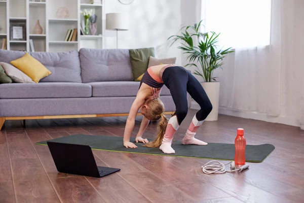 Sports jump rope. Reusable water bottle. Distant training with personal trainer. Child girl in sportswear watching online video on laptop and doing fitness exercises at home.