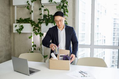 Asyalı bir adam işten kovuldu ve eşyaları karton kutuya koyuyor. Kovulma ve iş kaybı konsepti. İflas.