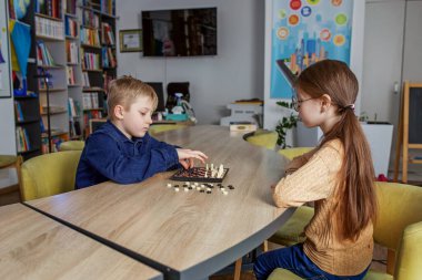 Beyaz çocuk ve kız satranç oynuyorlar, okulda masada birlikte oturuyorlar. Küçük arkadaş canlısı sınıf arkadaşları.