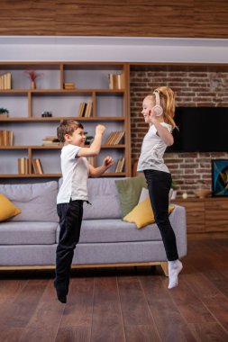 Çocuklar kulaklıkla müzik dinlerken evde zıplayıp dans ediyorlar. Eğleniyorum. Çocukluk ve aile kavramı.
