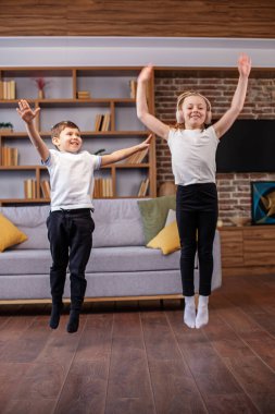 Çocuklar kulaklıkla müzik dinlerken evde zıplayıp dans ediyorlar. Eğleniyorum. Çocukluk ve aile kavramı.