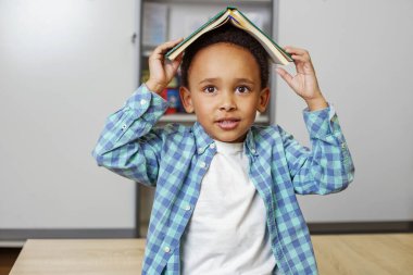 Kafasında kitap olan komik afro çocuk. Okula dönelim. Eğitim kavramı.