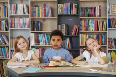 Sınıf arkadaşları sınıfta çalışır. Okula dönelim. Çok ırklı öğrenciler kütüphane veya sınıftaki masada ders çalışıp yazıyorlar..