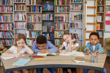 Sınıf arkadaşları sınıfta çalışır. Okula dönelim. Çok ırklı öğrenciler kütüphane veya sınıftaki masada ders çalışıp yazıyorlar..