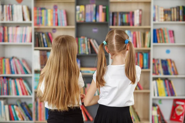 Two schoolgirls choose book in school library. Books on shelves in bookstore. Smart girls choose literature to read.