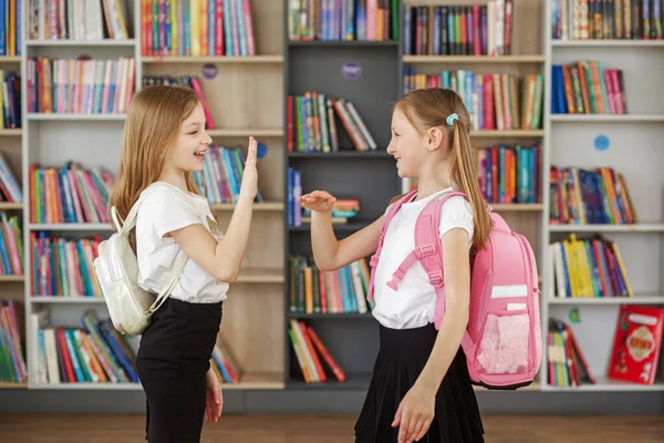 两个背着背包的女孩在暑假后在学校图书馆见面聊天 回学校去小学教育 — 图库照片