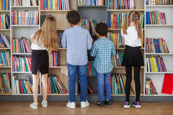 Vier Multietnische Kinderen Zoeken Boeken Buurt Van Boekenplanken Lezen Samen — Stockfoto