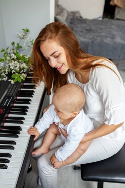 Anne ve küçük kızı piyano çalıyorlar. Bebek gelişimi. Duyusal deneyim. Beyin gelişimi. İlk yıllar.