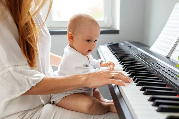 Mother and baby daughter playing piano. Baby development. Sensory experience. Brain development. Early years.