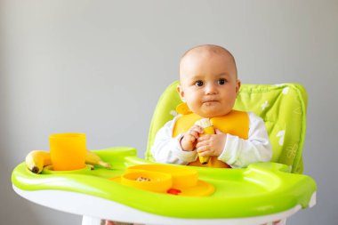 Bebek, yüksek sandalyede otururken kinoa lapası ve muz yiyor. Beslenme masası. Koltuk hazır. Taşınabilir bebek. Bebek güçlendirici. Taşınabilir katlama