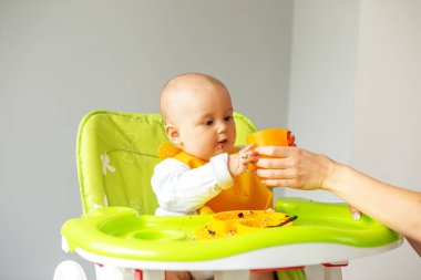 Bebek bakıcısı yeni doğmuş küçük bebeği mutfakta besler. Beslenme masası. Koltuk hazır. Taşınabilir bebek. Bebek güçlendirici. Taşınabilir katlama