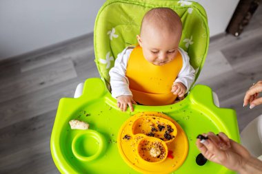 Bebek, yüksek sandalyede otururken kinoa lapası ve muz yiyor. Beslenme masası. Koltuk hazır. Taşınabilir bebek. Bebek güçlendirici. Taşınabilir katlama. Üst görünüm