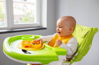 Bebek, yüksek sandalyede otururken kinoa lapası ve muz yiyor. Beslenme masası. Koltuk hazır. Taşınabilir bebek. Bebek güçlendirici. Taşınabilir katlama