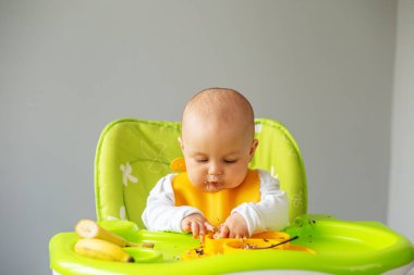 Bebek, yüksek sandalyede otururken kinoa lapası ve muz yiyor. Beslenme masası. Koltuk hazır. Taşınabilir bebek. Bebek güçlendirici. Taşınabilir katlama