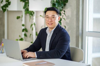 Girişimcilik, analitik ve finans konsepti. Çok ırklı personel. Ofiste çalışan mutlu Asyalı işadamı, dizüstü bilgisayar kullanıyor. İnsan kaynakları.