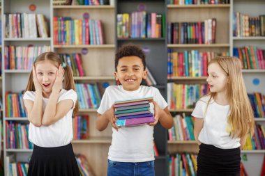 Çocuklar kütüphanede bir yığın kitap tutuyor. Çok ırklı sınıf arkadaşları eğleniyor. Dünya Kitap Günü. Günlük okumanın faydaları.