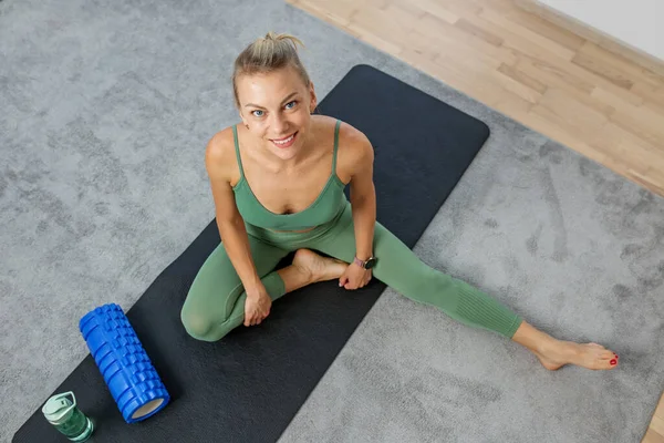 Millennial woman doing fitness and stretching in room using massage roll and mat. Training Concept. Copy space