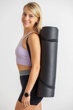 Minderli kız antrenmana hazırlanıyor. Beyaz arka planda yoga minderli ince vücutlu bir kadın. Uzayı kopyala Fitness, spor ve sağlıklı yaşam tarzı kavramı.