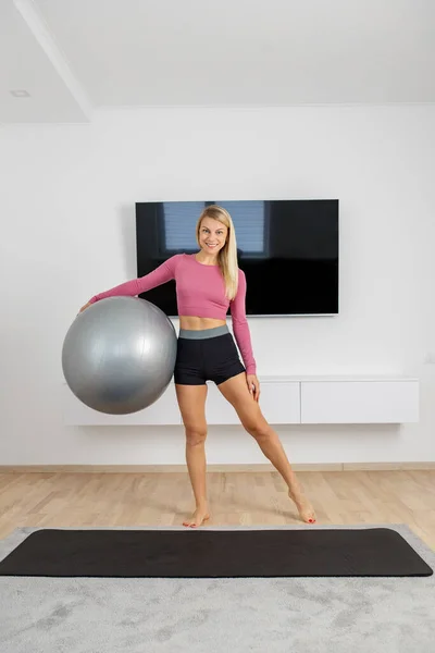 千禧年妇女在客厅的运动垫上带着健身球进行运动 运动和健康生活方式概念 — 图库照片
