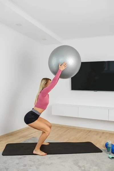 千禧年妇女在客厅的运动垫上带着健身球进行运动 运动和健康生活方式概念 — 图库照片