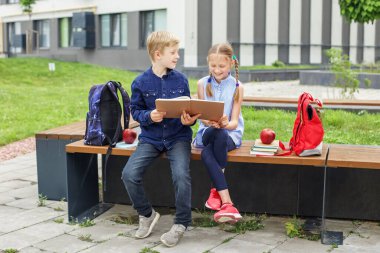 Okula dönelim. İki çocuk, erkek ve kız, birlikte kitap okuyorlar ve okul bahçesinde otururken konuşuyorlar..