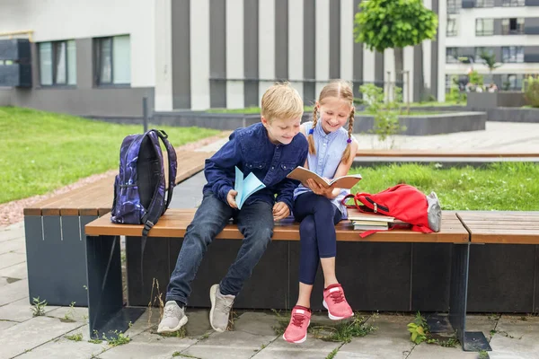 两个孩子一起看书 坐在学校院子里的长椅上聊天 玩得开心点回学校去 — 图库照片