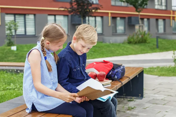 回学校去两个孩子 男孩和女孩 坐在学校院子里的长椅上看书 — 图库照片