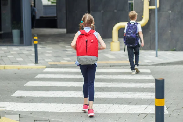 Traffic road rules. Child safety. School time. Back to school. Little pedestrians with backpacks walk to school and cross road at crosswalk.