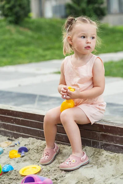 stock image Little girl playing in sandbox at playground outdoors. Toddler playing with sand molds and making mudpies. Outdoor creative activities for kids.