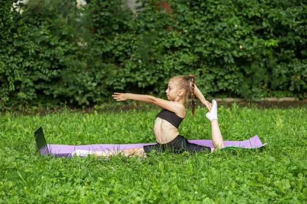 Healthcare concept. Rhythmic gymnastics. Child does outdoor sports exercises using fitness mat. Girl is doing gymnastics