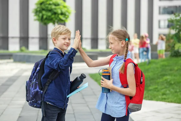 Two children with backpacks met near school. Back to school. High five. Meeting friends. Beginning of school lessons. Reusable water bottle
