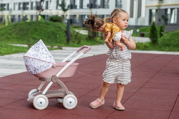 Little girl with doll in stroller. Two years old. Developmental milestones. Early years