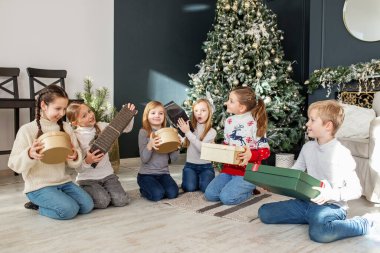 Mutlu Noeller ve mutlu tatiller. Evdeki eğlence partisinde Noel hediyelerini değiş tokuş ettikten sonra bir grup güler yüzlü çocuk oturma odasında yerde oturuyor.