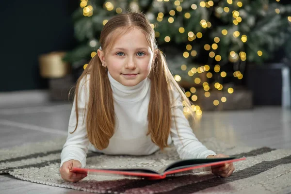 Smiling child reads book in room. Concept New Year, Merry Christmas, holiday, vacation, winter, childhood. Cozy home.