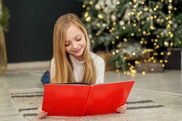 Smiling child reads book in room. Concept New Year, Merry Christmas, holiday, vacation, winter, childhood. Cozy home.