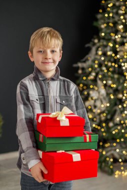 Elinde hediye kutuları olan bir çocuk Noel ağacı arka planında. Kavram Yeni Yıl, Mutlu Noeller, tatil, kış, çocukluk.
