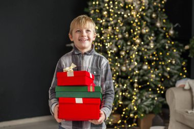 Elinde hediye kutuları olan bir çocuk Noel ağacı arka planında. Kavram Yeni Yıl, Mutlu Noeller, tatil, kış, çocukluk.