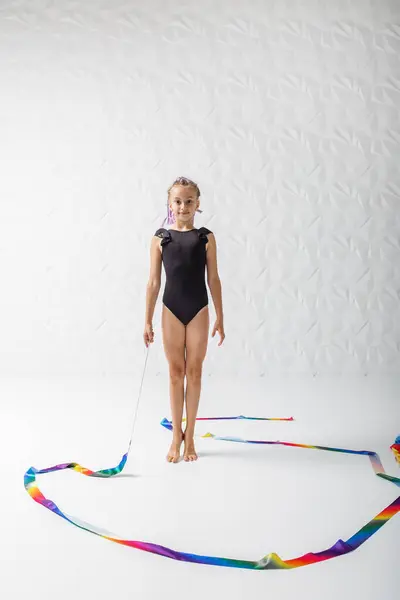 Rhythmic gymnastics. Preteen girl athlete rhythmic gymnastic in black suit does exercise with art ribbon. Children's professional sports. Copy space