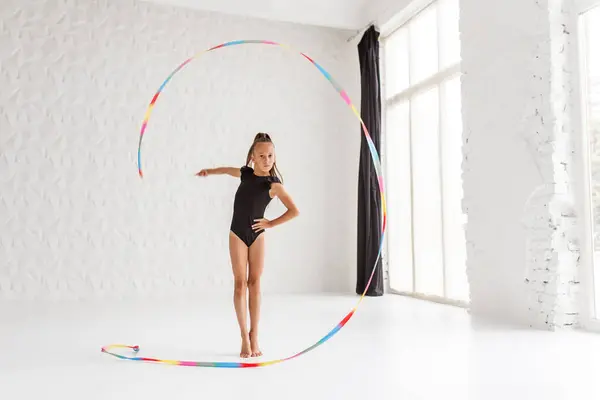 Rhythmic gymnastics. Preteen girl athlete rhythmic gymnastic in black suit does exercise with art ribbon. Children\'s professional sports. Copy space