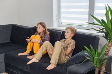 Çocuklar kanepede oturup ilginç TV filmleri izliyorlar. TV kumandası tutan kız. Okuldan sonra dinlen..