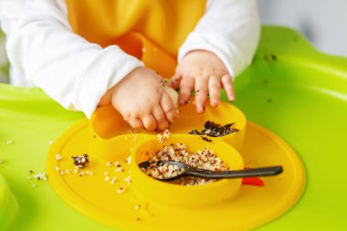 Bebek, yüksek sandalyede otururken kinoa lapası ve muz yiyor. Beslenme masası. Koltuk hazır. Taşınabilir bebek. Bebek güçlendirici. Taşınabilir katlama