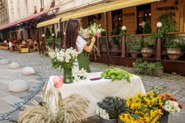 Yeşil benekli önlüklü odaklı çiçekçi büyüleyici sokak köşesinde renkli çiçek seçimi düzenler.