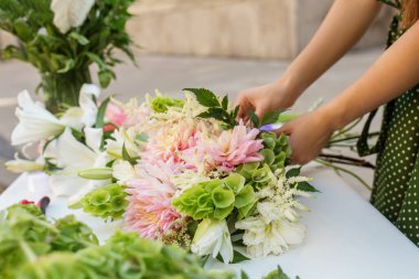 Çiçekçinin ellerine dikkatlice son rötuşları yaparken canlı pembe yıldız çiçekleri ve yemyeşil çiçeklere dokunuyor..