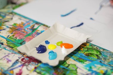 Renkli arka planda beyaz palette sergilenen canlı akrilik boyalar devam etmekte olan sanatı simgeliyor..