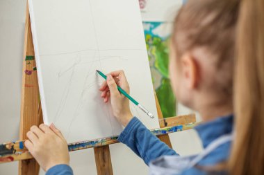 Odaklanmış öğrenci, sanat sınıfı ortamında boş tuvale ilk çizimlerini dikkatlice çiziyor.