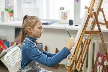 Focused student carefully sketching initial outlines of drawing on blank canvas in an art class environment clipart